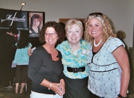 Three women posing for a picture in front of a wall.