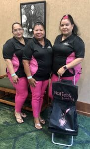 Three women in black and pink outfits standing next to a bag.