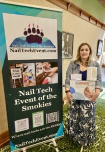 A woman standing next to a sign that says nail tech event of the smokies.