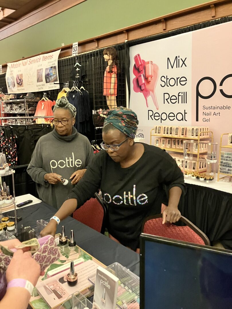 2 black ladies working inside The Pottle booth at the Smokies Nail Show