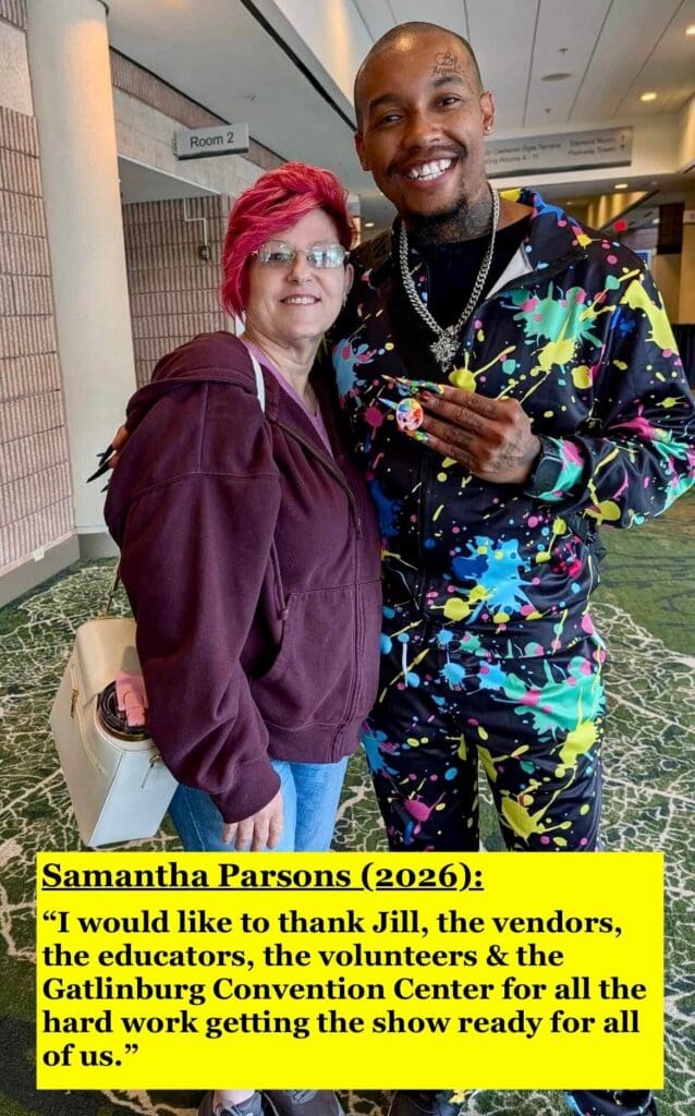 white woman with red hair standing beside colorfully dressed black man wearing long nails